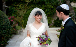 Sephardic bride with veil and flowers with groom looking at her