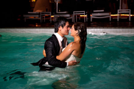 Wedding couple kissing after jumping in the pool with their clothes on