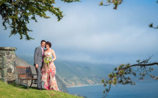 Wedding couple standing on grassy hill overlooking blue ocean