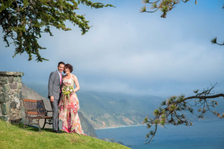 Wedding couple standing on grassy hill overlooking blue ocean
